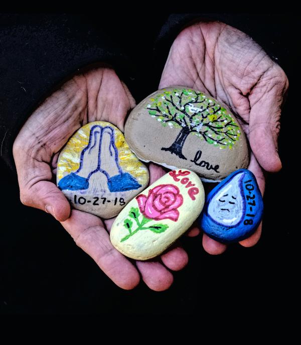 Hands at prayer holding painted stones reading “love” and “10-27-18”